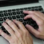 Close-up of hands typing on a laptop keyboard, representing searching or managing personal information online.