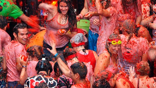 Revelers at La Tomatina festival in Buñol, Spain, laughing and throwing smashed tomatoes at each other, covered in red pulp, embodying the joyful chaos and unique spirit of the world’s biggest tomato fight.