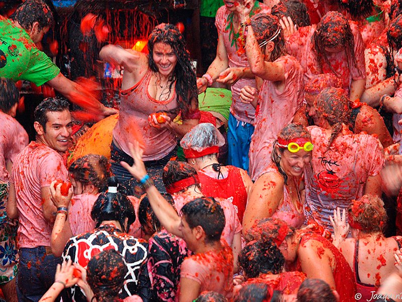 Revelers at La Tomatina festival in Buñol, Spain, laughing and throwing smashed tomatoes at each other, covered in red pulp, embodying the joyful chaos and unique spirit of the world’s biggest tomato fight.