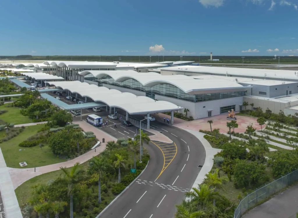 Aerial view of Lynden Pindling International Airport in Nassau, Bahamas, featuring the modern terminal, palm trees, and runway under a clear blue sky.