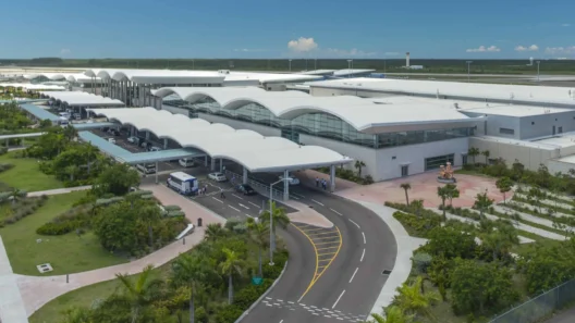 Aerial view of Lynden Pindling International Airport in Nassau, Bahamas, featuring the modern terminal, palm trees, and runway under a clear blue sky.