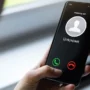 A person holding a smartphone with an incoming call from an unknown number, displayed on the screen with options to accept or decline the call.
