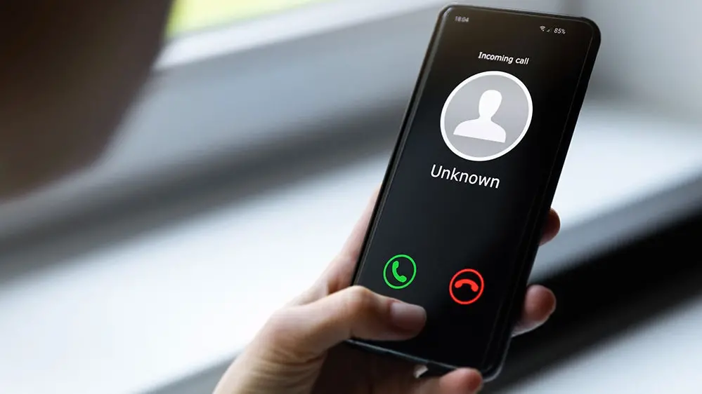 A person holding a smartphone with an incoming call from an unknown number, displayed on the screen with options to accept or decline the call.