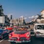 Classic vintage cars driving through the historic streets of Havana, Cuba, with colorful colonial buildings and palm trees in the background