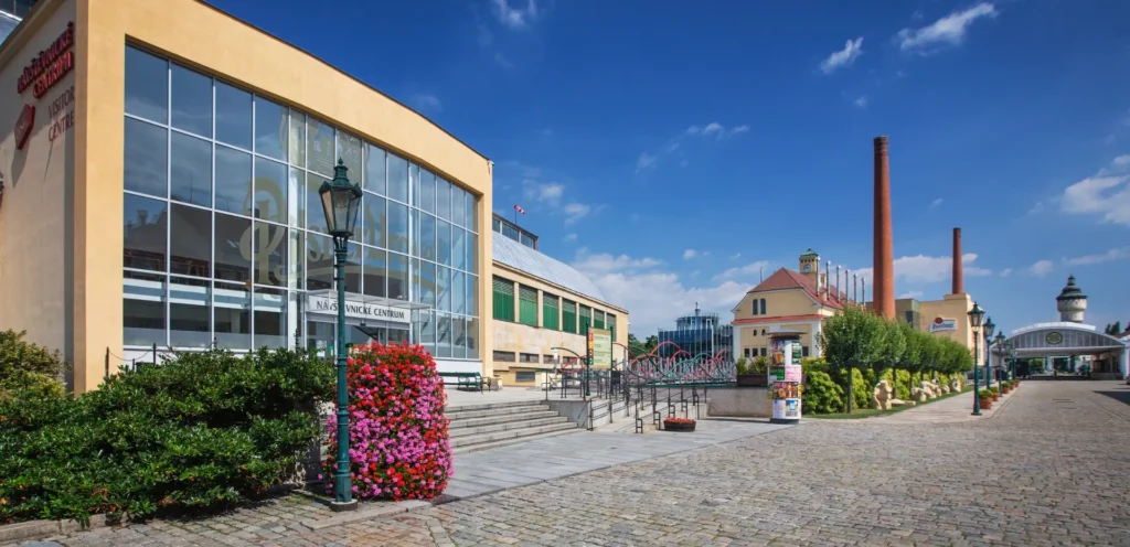 Pilsner Urquell Visitor Centre exterior with brewery buildings, red brick chimneys, and clear blue sky in Pilsen, Czech Republic