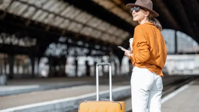 A smiling female traveler with a suitcase and coffee, ready to explore Prague using public transport.