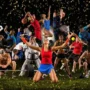A dynamic collage of athletes playing soccer, basketball, tennis, weightlifting, martial arts and other sports in a stadium under bright lights with confetti flying.