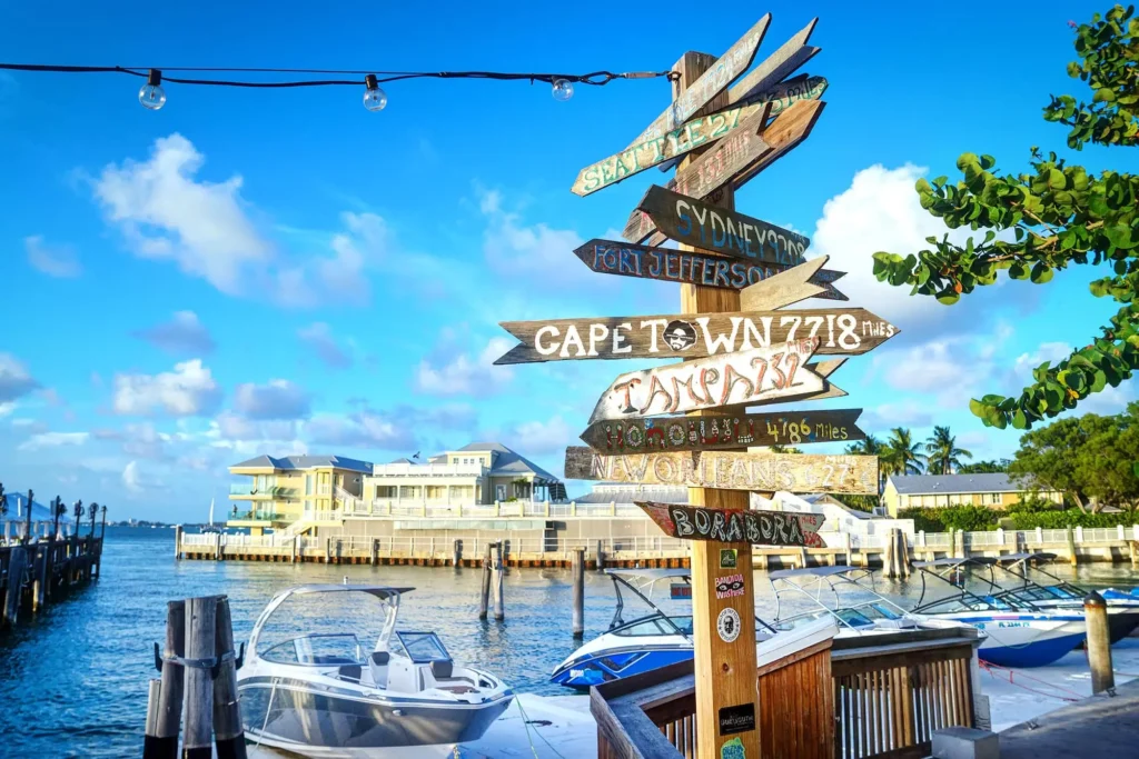 Colorful direction sign at a marina in Key West, pointing to cities around the world under a bright blue sky.