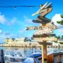 Colorful direction sign at a marina in Key West, pointing to cities around the world under a bright blue sky.