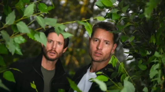 Colter Shaw (played by Justin Hartley) and another character looking through leaves in a tense forest scene from Tracker Season 3.