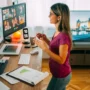A woman working from her home office, leading a video call with colleagues on dual monitors, surrounded by charts, documents, and a London bridge photo on the TV in the background – a modern remote work setup.