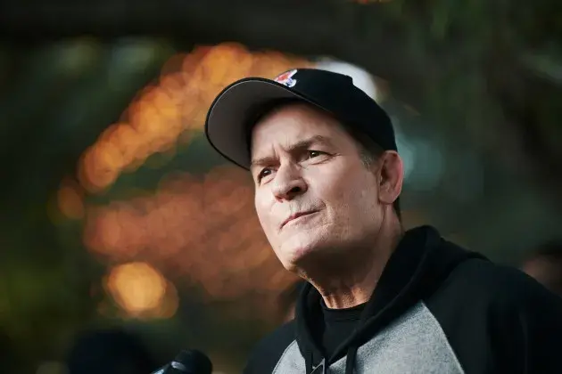 Charlie Sheen looking thoughtful outdoors, wearing a black hoodie and baseball cap, reflecting on his life in the new Netflix documentary.