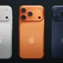 Three Apple iPhone 17 models in silver, orange, and dark blue colors, showcasing the redesigned camera layout and minimalist rear design.