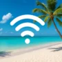 A tropical beach in the Bahamas with turquoise sea, white sand, and palm trees, overlaid with a modern WiFi signal icon representing internet connectivity in paradise.