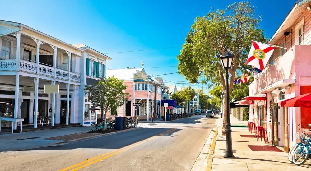 Colorful pastel buildings, bikes, and flags lining lively Duval Street in the heart of Key West on a sunny afternoon.