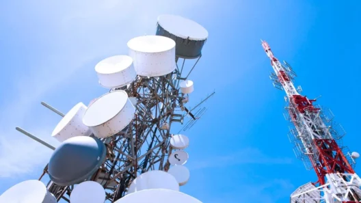Two large internet and cellular towers packed with antennas and satellite dishes under a clear blue sky, symbolizing ISP data traffic and monitoring.