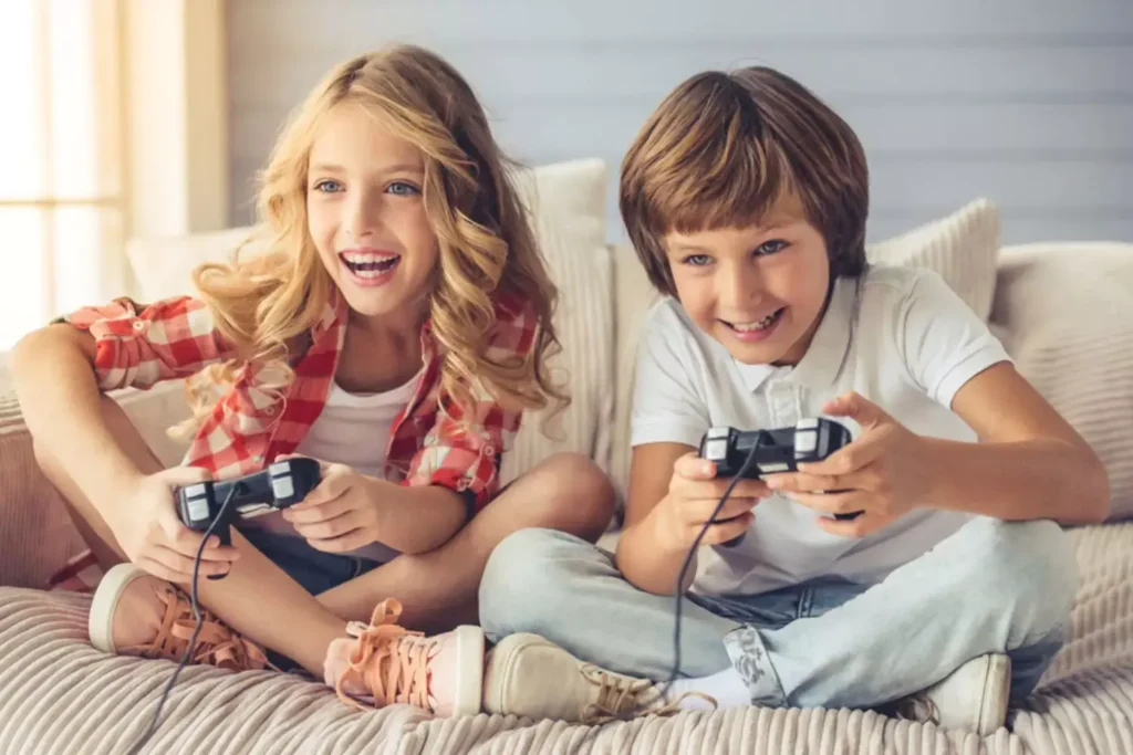 Two children sitting on a couch happily playing video games with wired controllers