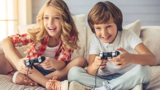 Two children sitting on a couch happily playing video games with wired controllers