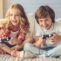 Two children sitting on a couch happily playing video games with wired controllers