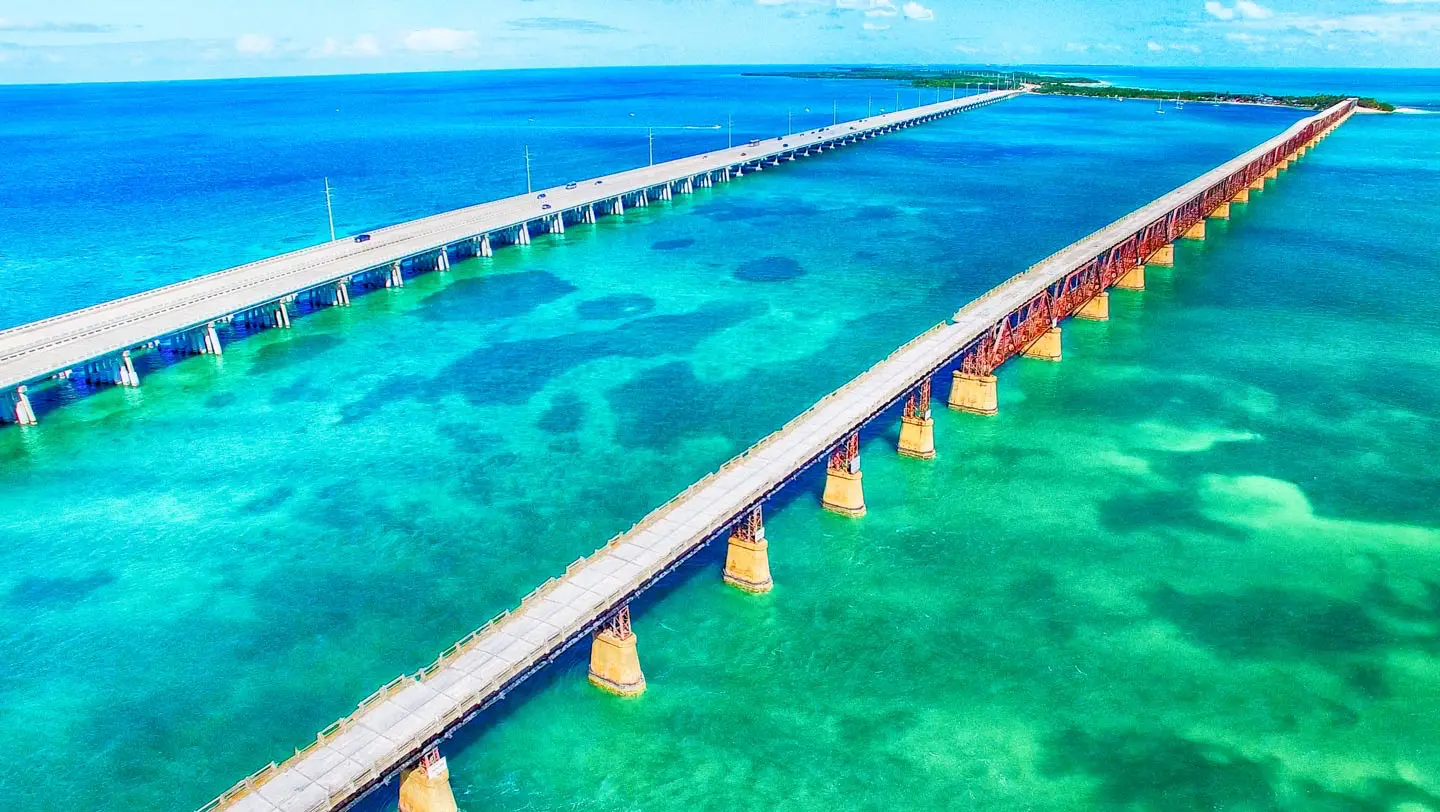 A vibrant aerial view of the Old Seven Mile Bridge and new Overseas Highway slicing through blue-green ocean near Marathon.