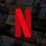 Netflix logo in front of a blurred background showing popular shows and movies from the streaming library, symbolizing hidden categories and secret codes to unlock the full collection