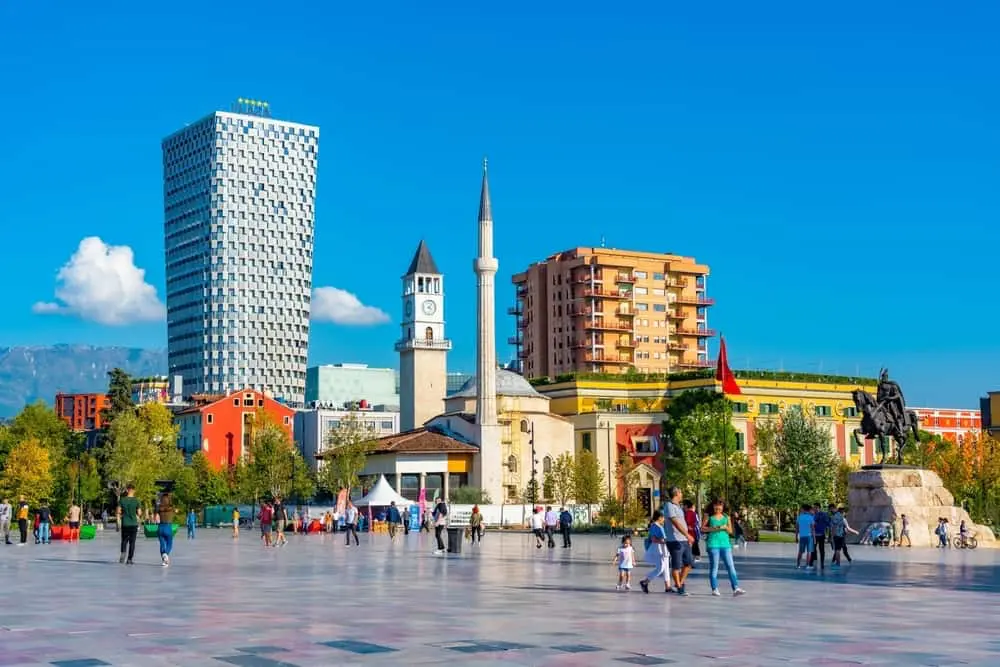 Skanderbeg Square in Tirana with the Clock Tower, Et’hem Bey Mosque, modern high-rises, and the statue of national hero Skanderbeg under a clear blue sky