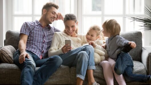 Family chilling on the couch, laughing at something on a phone — classic screen time together moment.
