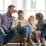 Family chilling on the couch, laughing at something on a phone — classic screen time together moment.