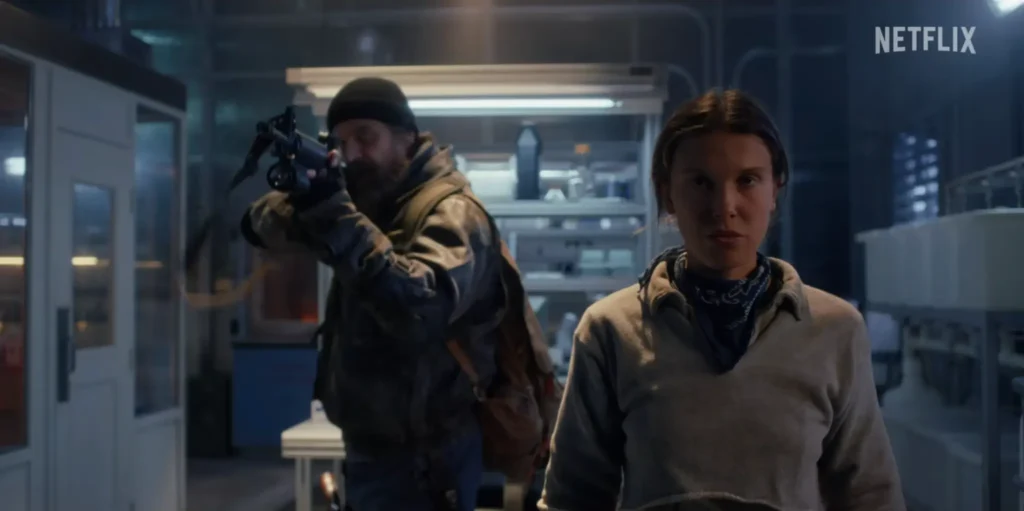 stranger-things-5-hopper-eleven-lab_scene_ads | Venclikovi.com Hopper aims his gun while Eleven walks forward in a tense Hawkins lab moment.