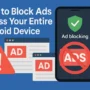 Illustration showing a centered Android phone with a green shield and "Ad blocking" text on its screen. A red "no ads" symbol overlays it. On the left, browser windows labeled "AD" and a red warning triangle emphasize blocked ads. The background is solid blue with balanced spacing and no elements touching the edges. Text above reads: "How to Block Ads Across Your Entire Android Device".