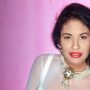 Selena Quintanilla close-up portrait with bold red lipstick and statement jewelry, set against a pink background—timeless beauty and confidence.