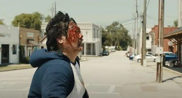 weapons-2025-bleeding-man-small-town-street | Venclikovi.com Bloodied man stumbles through a deserted small town street in a scene from Weapons 2025