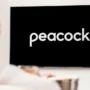 Woman watching Peacock TV on a modern flat-screen television in a cozy home setting, viewed from behind