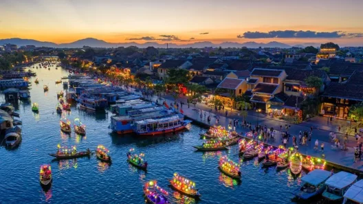 Lantern-lit boats on the river in Hội An, Vietnam at sunset, with crowds and old town buildings in view.