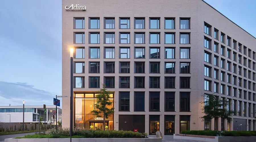 Adina Apartment Hotel Cologne | Venclikovi.com The modern brick exterior of the Adina Apartment Hotel at dusk, featuring a large glass entrance and clean architectural lines.