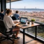Digital nomads working on laptops in a modern co-working space with a stunning panoramic view of Lisbon’s terracotta roofs and the iconic bridge.