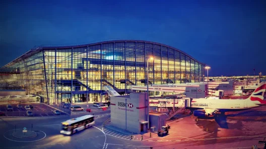 Exterior night view of London Heathrow Airport Terminal 5, showcasing the terminal-linked infrastructure and a British Airways plane at the boarding gate.