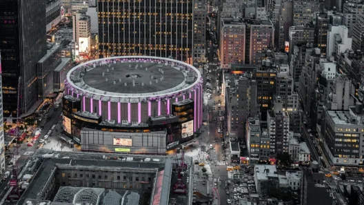 Aerial night view of Madison Square Garden lit in purple, surrounded by Midtown Manhattan skyscrapers and yellow taxis, the world's most famous arena above Penn Station NYC.