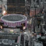 Aerial night view of Madison Square Garden lit in purple, surrounded by Midtown Manhattan skyscrapers and yellow taxis, the world's most famous arena above Penn Station NYC.