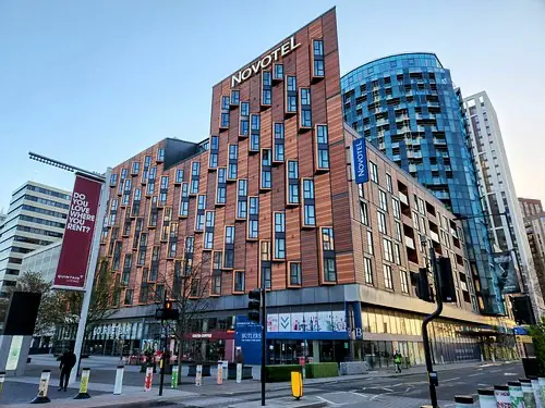 Novotel London Wembley | Venclikovi.com An architecturally unique hotel building with a textured wood-panel facade and protruding window boxes, located on a street corner in Wembley Park.