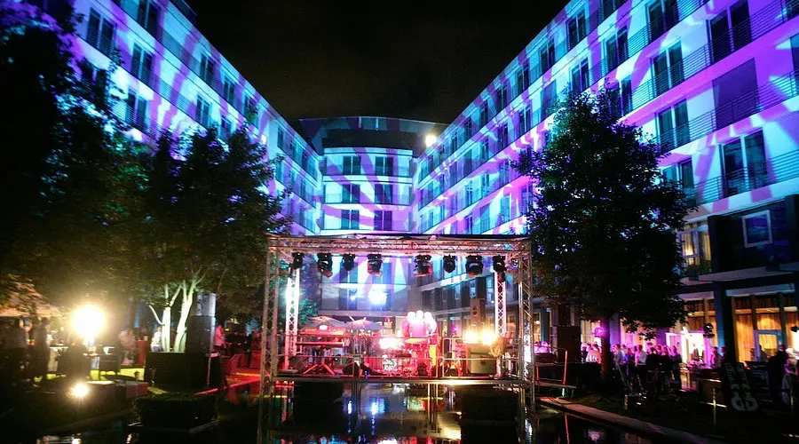Radisson Blu Hotel Cologne | Venclikovi.com An outdoor evening event at the Radisson Blu Hotel, featuring colorful light projections on the building walls and a small stage.