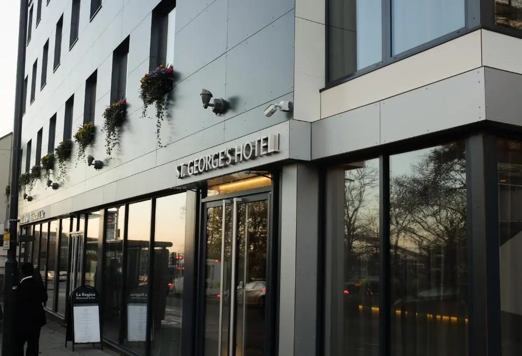 St Georges Hotel Wembley | Venclikovi.com The exterior entrance of St George's Hotel featuring large glass windows, a grey paneled facade, and flower boxes under the windows.
