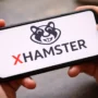 Smartphone held in hands showing the xHamster logo on the screen, illustrating access to adult content on a mobile device